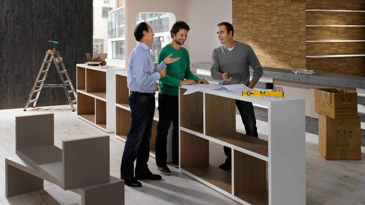 Planungsgespräch für Messe-/Showroomaufbau Planungsgespräch für Messe-/Showroomaufbau zwischen drei Männern mit unfertigen Mobiliar im Hintergrund
